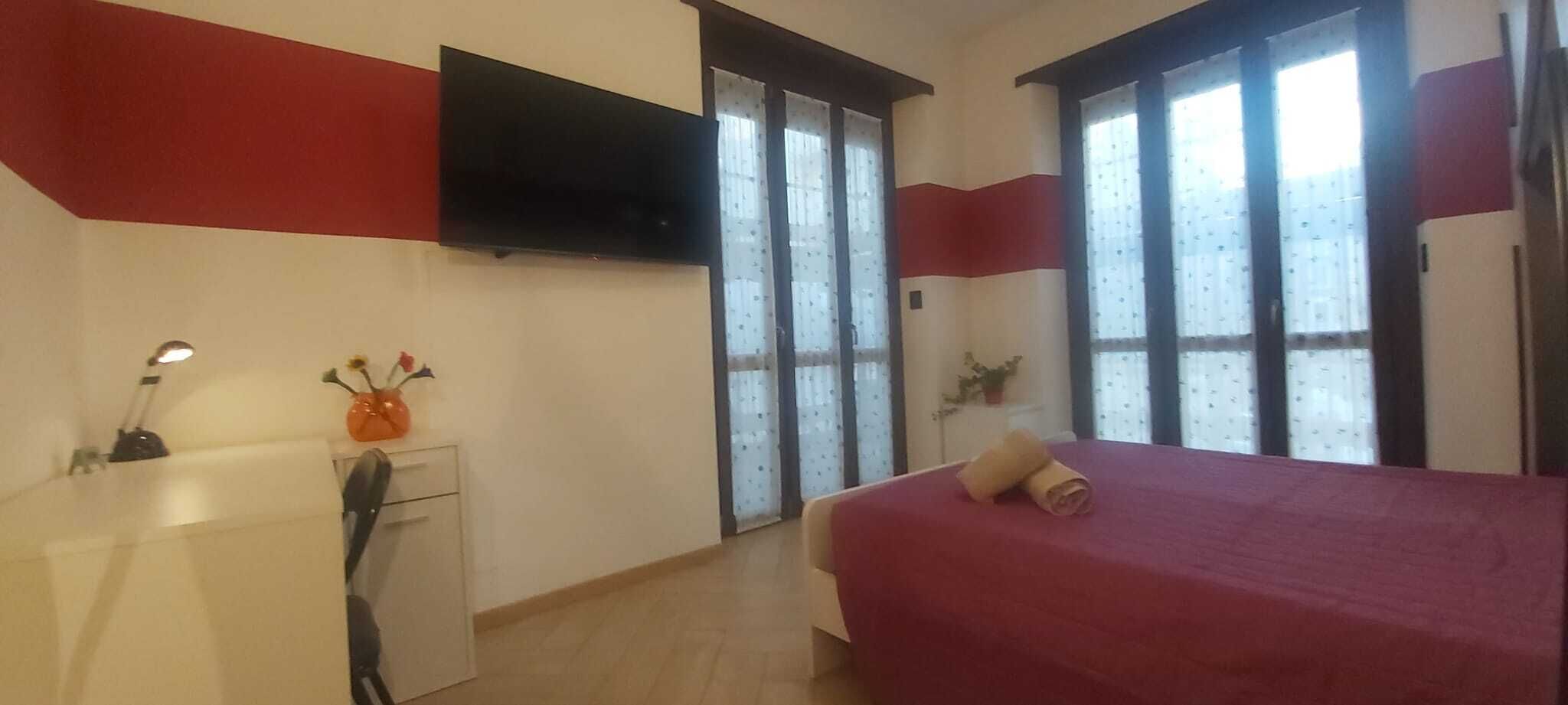 A bedroom with a bed, a desk, a TV, and a window.