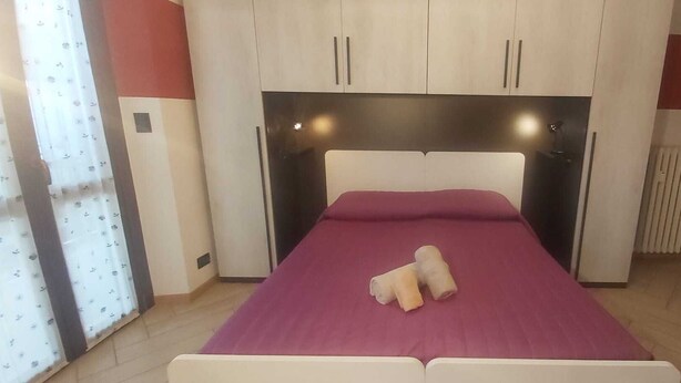 A bed with a headboard, a pair of towels, and a window with curtains. - Appartamento confortevole con doccia idromassaggio (Torino)