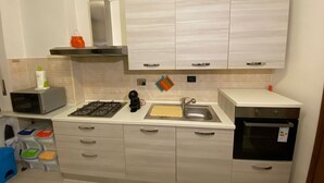 A modern kitchen with a gas stove, stainless steel sink, and white cabinetry. - Appartamento confortevole con doccia idromassaggio (Torino)