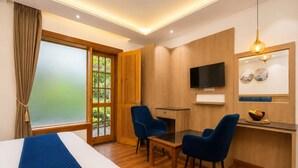 Ein Hotelzimmer mit einem Bett, einem Schreibtisch mit zwei Stühlen, einem Fernseher und einem großen Fenster mit Vorhängen.