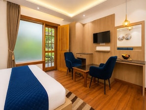 Une chambre d’hôtel avec un lit, un bureau avec deux chaises, une télévision et une grande fenêtre avec des rideaux.