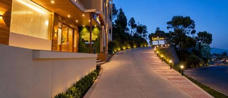 A hotel entrance with a pathway leading to the building, a signboard, and a well-lit exterior.