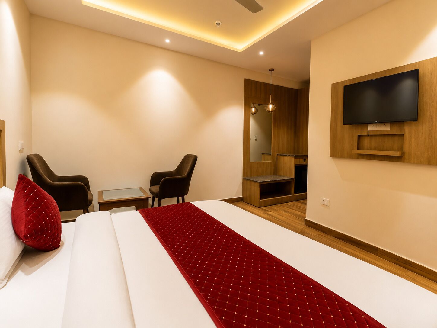 A hotel room with a bed, two chairs, a small table, a TV, and a mirror.