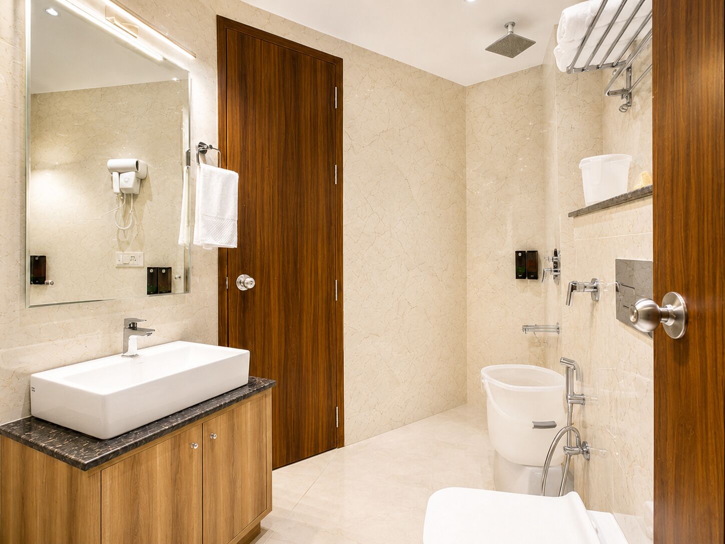 Un baño moderno con tocador de madera, un espejo grande, un lavabo blanco, un inodoro y una zona de ducha.