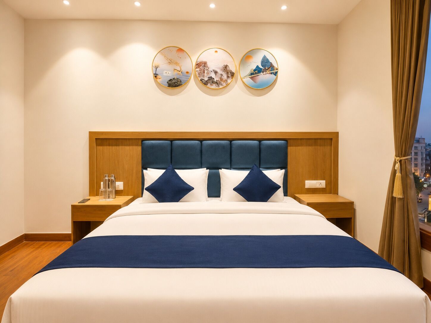 A hotel room with a large bed, wooden headboard, two bedside tables, and three wall-mounted artworks.