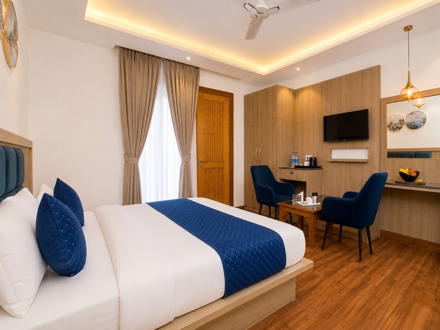 A hotel room with a bed, a desk, a chair, a television, and a ceiling fan.