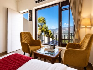 A hotel room with a bed, two armchairs, a small table, a balcony with a view of mountains and trees, and a window with curtains. - Hotel Luxeevista By Navodayans  (Dalhousie)