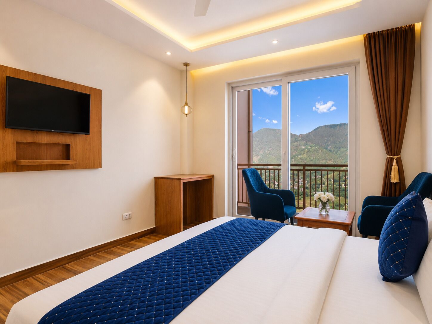 Une chambre d’hôtel avec un lit, un téléviseur fixé au mur, un balcon avec des chaises et une vue sur les montagnes.