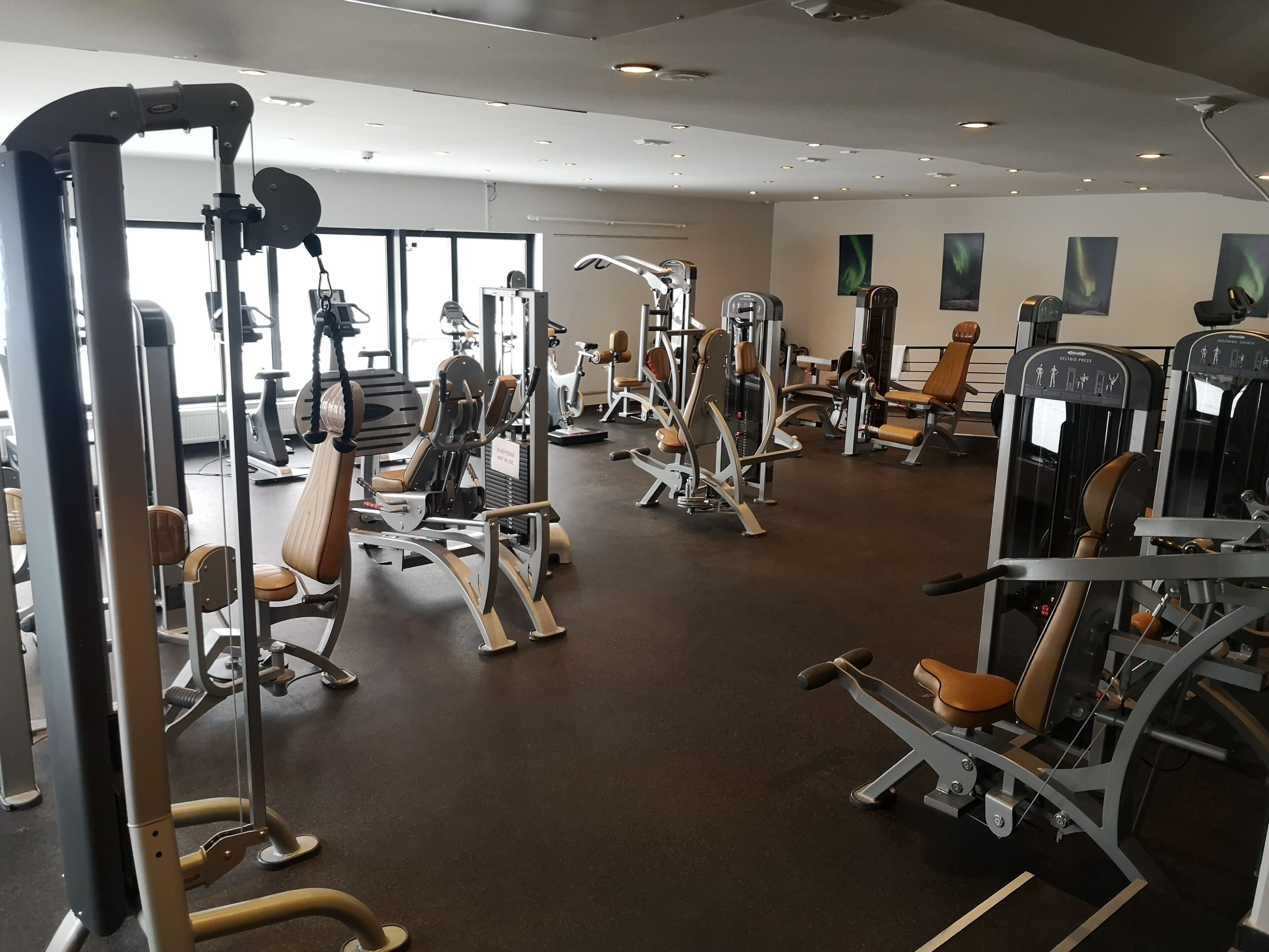 A gym with various exercise machines, a large window, and a wall-mounted television.