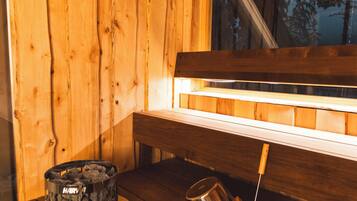 Interior de una cabaña de madera con un banco, una ventana y una chimenea con un recipiente y una taza de metal.