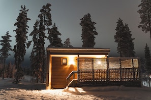 A wooden cabin with a staircase, a window, and a snow-covered landscape.