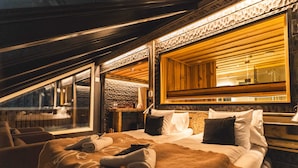 Een gezellige, goed verlichte slaapkamer met een groot bed, een raam en een houten plafond.