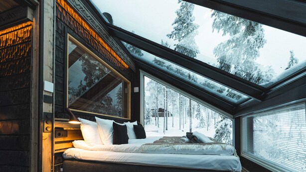 Een slaapkamer met een groot raam, een bed en uitzicht op met sneeuw bedekte bomen.