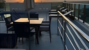 Kattoterassi, jossa on pöytä ja tuoleja, suuri aurinkovarjo ja näkymä auringonlaskuun.