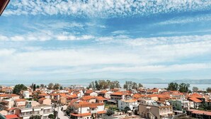 Un pueblo costero con edificios de techo rojo, cielo despejado y montañas a lo lejos.