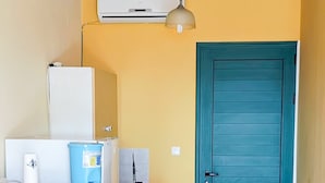 Een keuken met een wit aanrecht, een blauwe prullenbak, een wit apparaat en een blauwgroene deur.