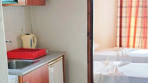 Ein gemütlicher Raum mit Küchenzeile, einem Bett und einem karierten Vorhang sowie einem gefliesten Boden.
