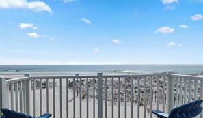 A beach view from a balcony with a white railing, blue chairs, and a sandy beach with a fence. - Horizon 22 - Beach Pool Dining Fun (Gulf Shores)