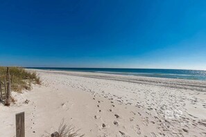 En strand med sand, ett trästaket och en klarblå himmel.