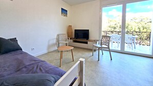 A room with a bed, a TV, a desk, and a balcony with chairs. - The "Le Cosy" Apartment – Shared Pool (La Tranche-sur-Mer)