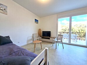 A room with a bed, a TV, a desk, and a balcony with chairs. - The "Le Cosy" Apartment – Shared Pool (La Tranche-sur-Mer)