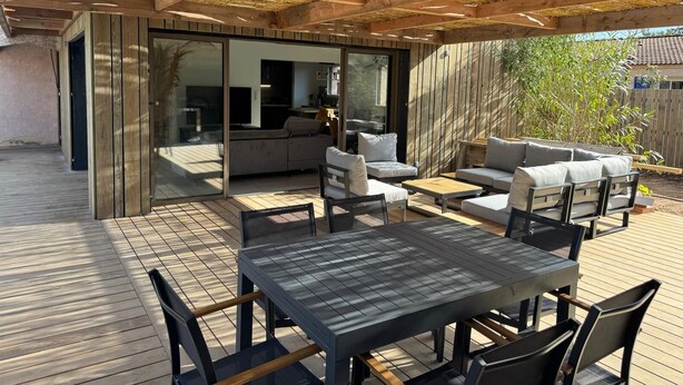 Eine Terrasse im Freien mit Holzdeck, einem Esstisch mit Stühlen und einer Sitzecke mit einer Couch.
