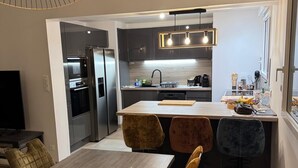 Eine moderne Küche mit Kochinsel, integrierten Geräten und einem Essbereich mit Holztisch und gepolsterten Stühlen.