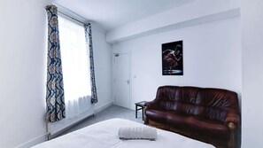 A bedroom with a bed, a brown leather sofa, a door, and a framed picture on the wall. - Spacious Home Near Seafront Perfect For Groups (Redcar)