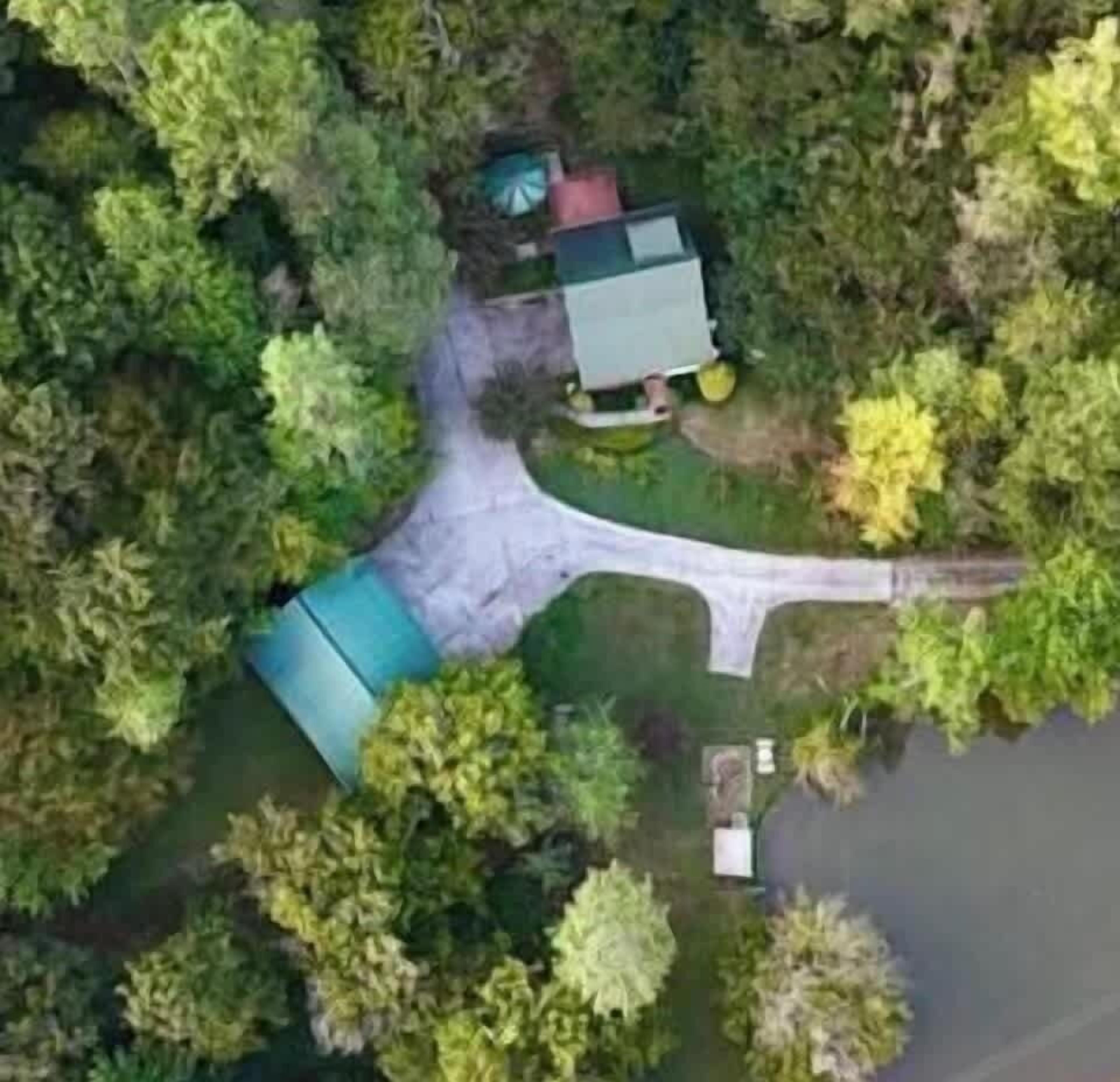 An aerial view of a property with a green-roofed building, a driveway, and surrounding trees.