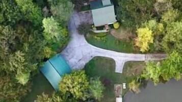 An aerial view of a property with a green-roofed building, a driveway, and surrounding trees.