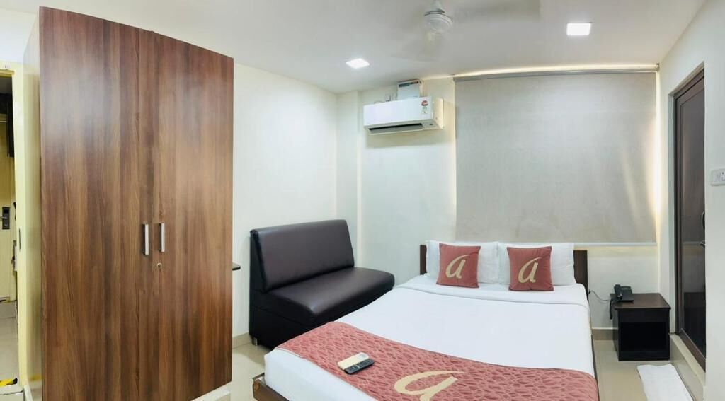 Quarto com cama, cadeira preta, guarda-roupa e mesa de cabeceira.