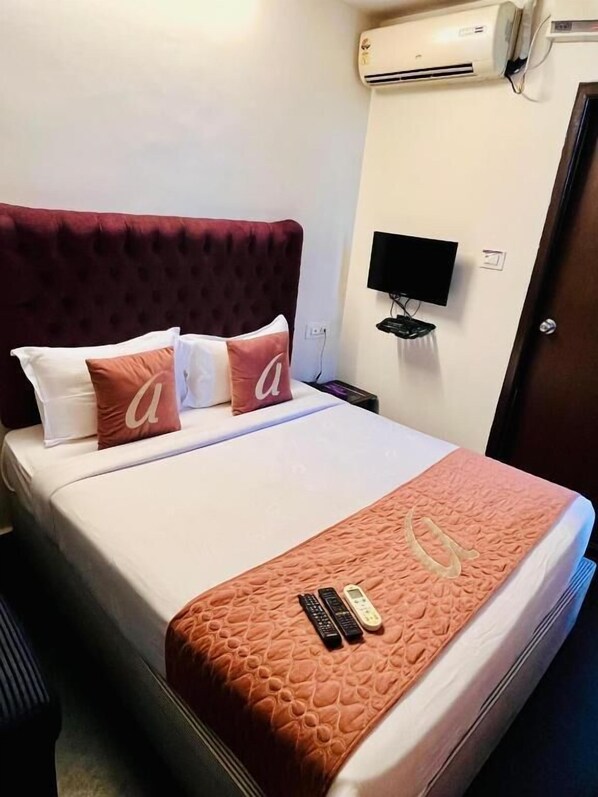 A hotel room with a bed, a TV, an air conditioning unit, and a door. - Astra Hotel and Suites Hsr 1st Sector (Bengaluru)