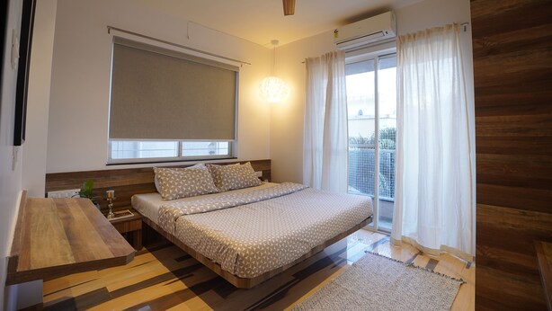 Un dormitorio con una cama, un ventilador de techo, una ventana con cortinas y suelo de madera.