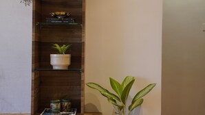 Estantería de madera con un reloj, libros y objetos decorativos. Una planta grande en maceta se encuentra al lado de la estantería.