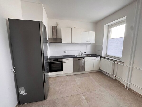 A modern kitchen with white cabinets, a stainless steel refrigerator, and a window providing natural light.