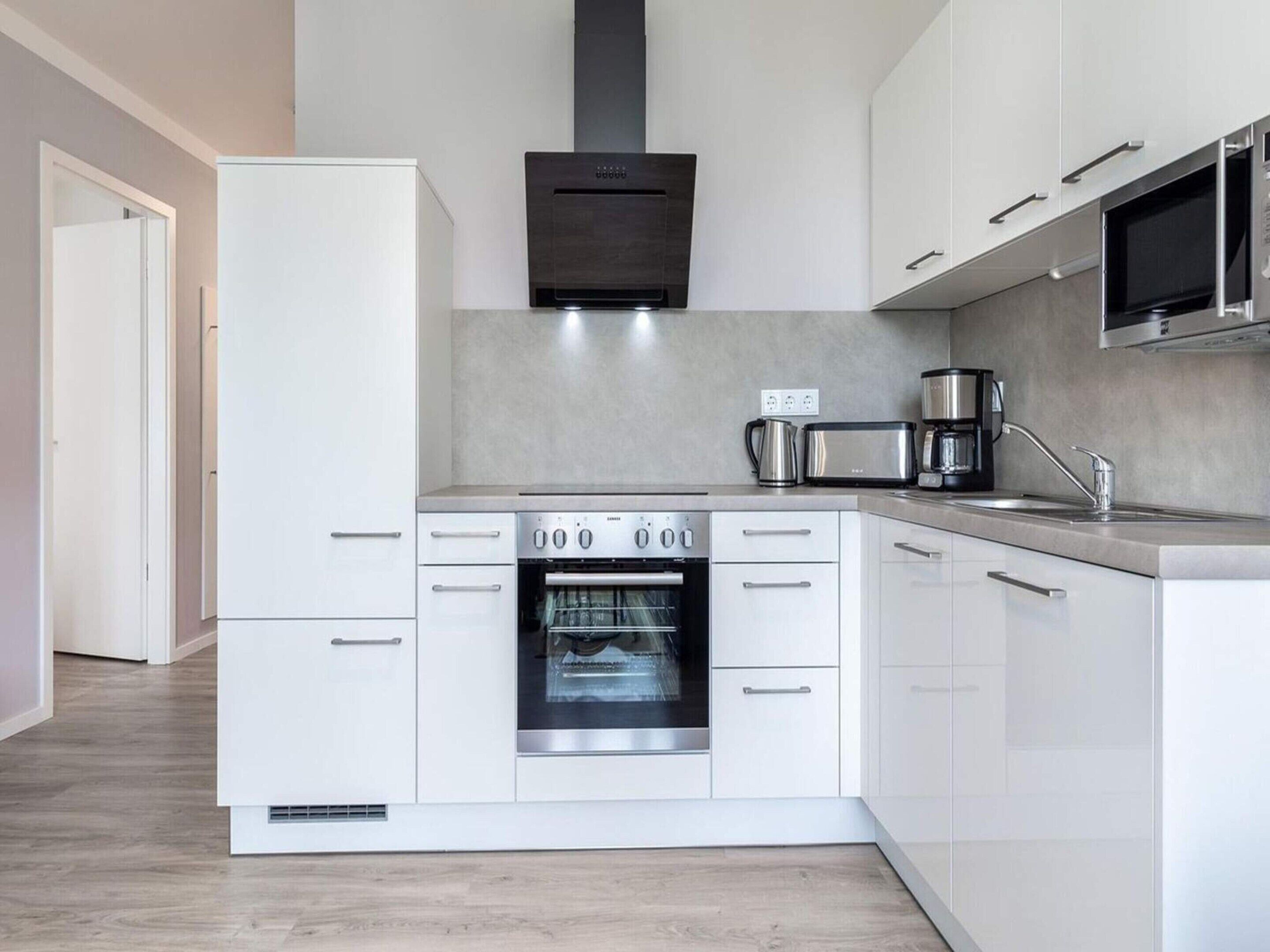 Una cocina moderna con armarios blancos, horno empotrado, microondas y cafetera.