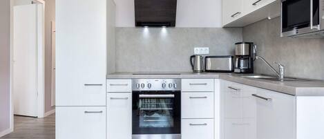 Una cocina moderna con armarios blancos, horno empotrado, microondas y cafetera.