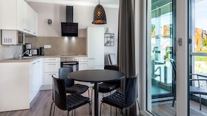 A modern kitchen with white cabinets, a black stove, and a dining area with a round table and four chairs. - Travemunde Beach Retreat (Lübeck)
