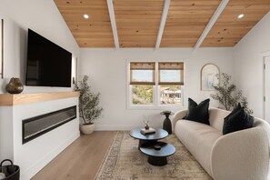 Una sala de estar moderna con un televisor de pantalla plana, chimenea, sofá, mesa de centro y un ventanal grande.
