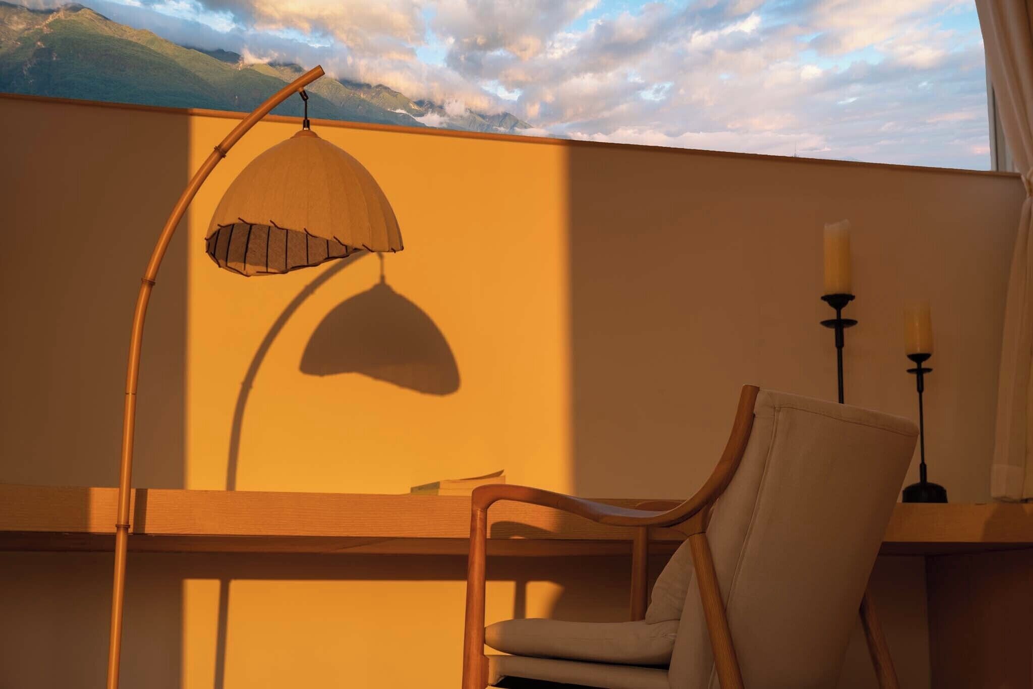 Une pièce avec vue sur les montagnes, un bureau en bois, une chaise, une lampe suspendue et deux chandeliers.
