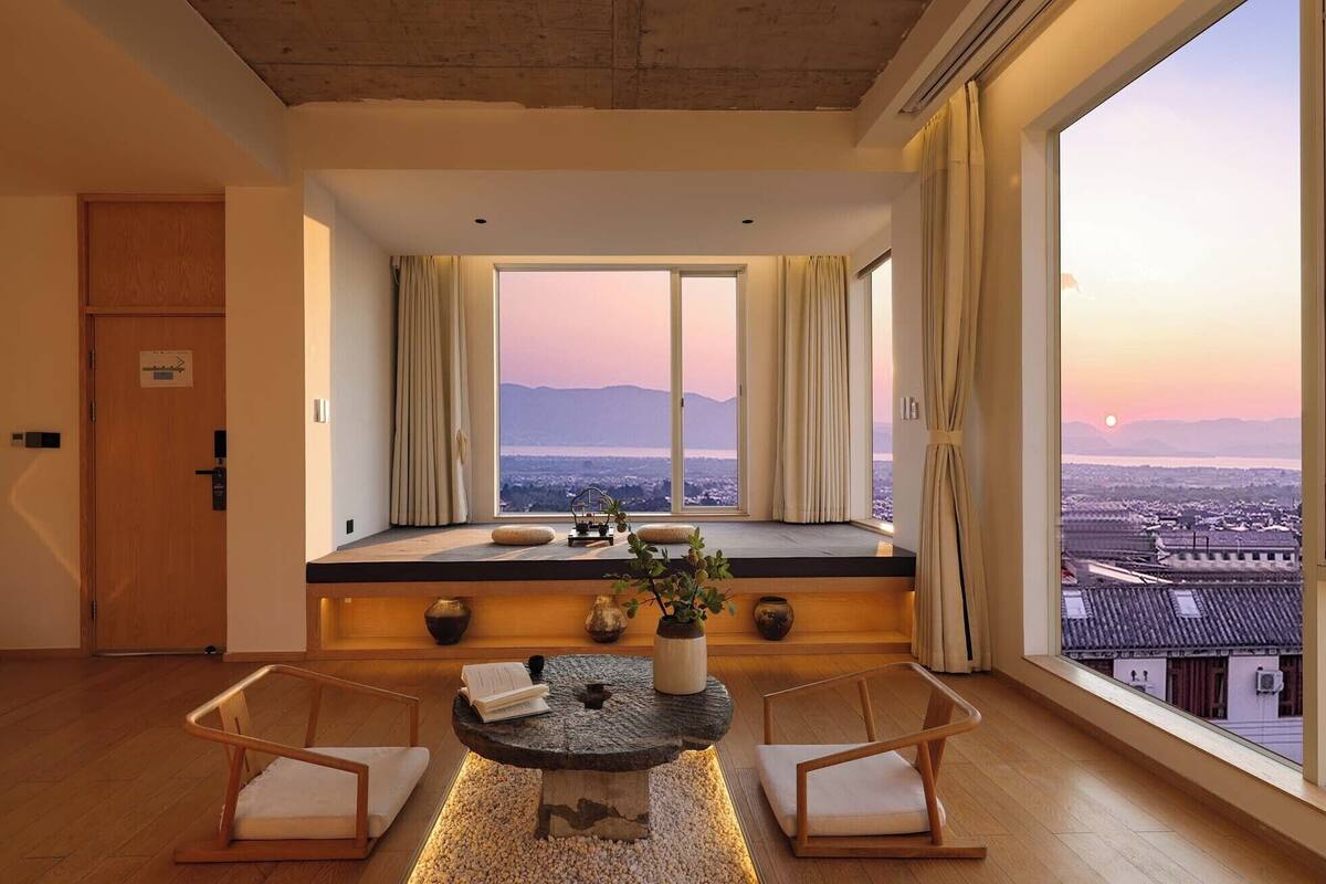 A room with a large window, a stone table, two chairs, and a view of a cityscape.