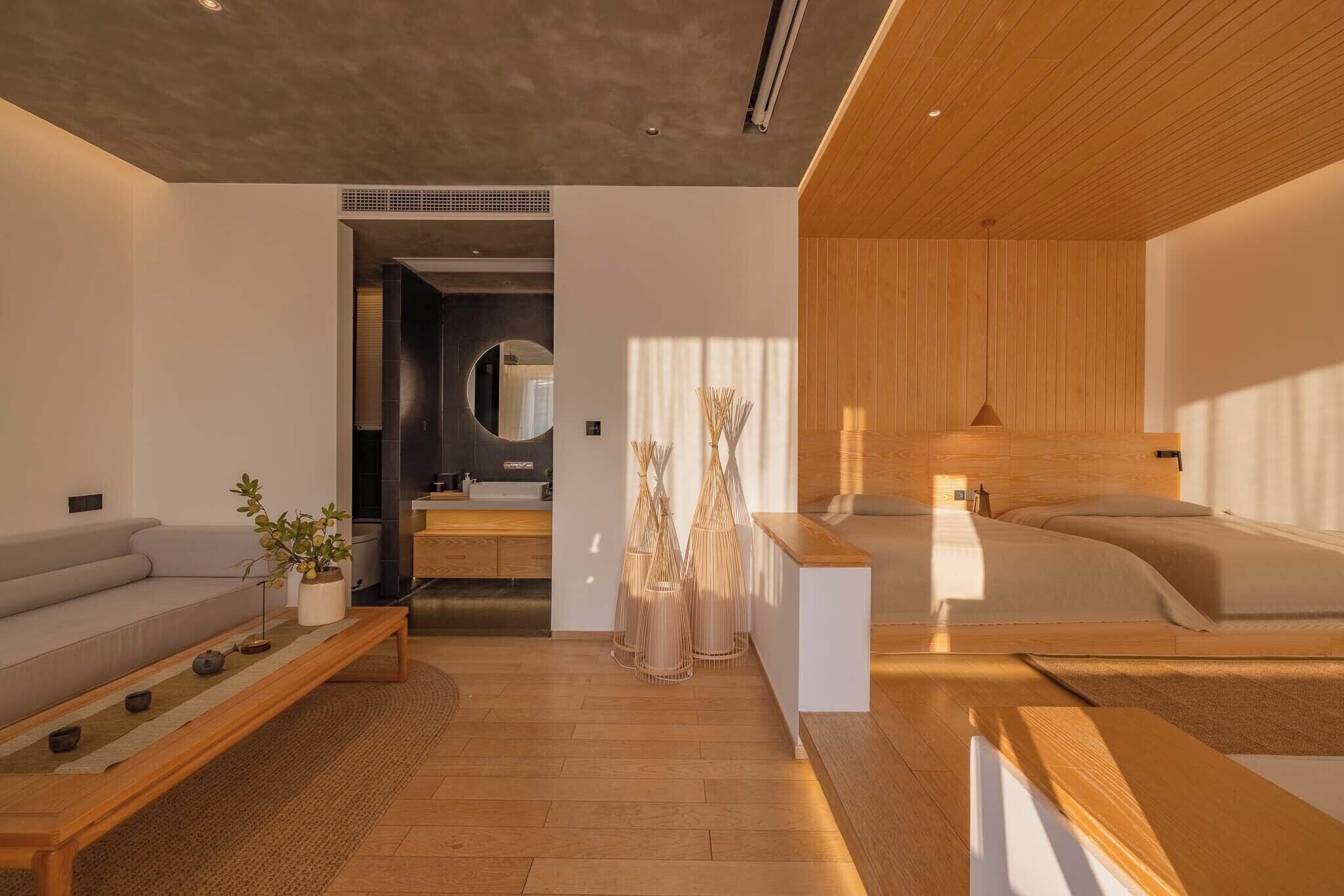 A modern hotel room with a wooden ceiling, a sofa, a bedside table, a bed, and a small bathroom area.