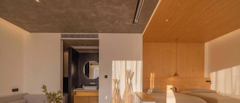 A modern hotel room with a wooden ceiling, a sofa, a bedside table, a bed, and a small bathroom area.