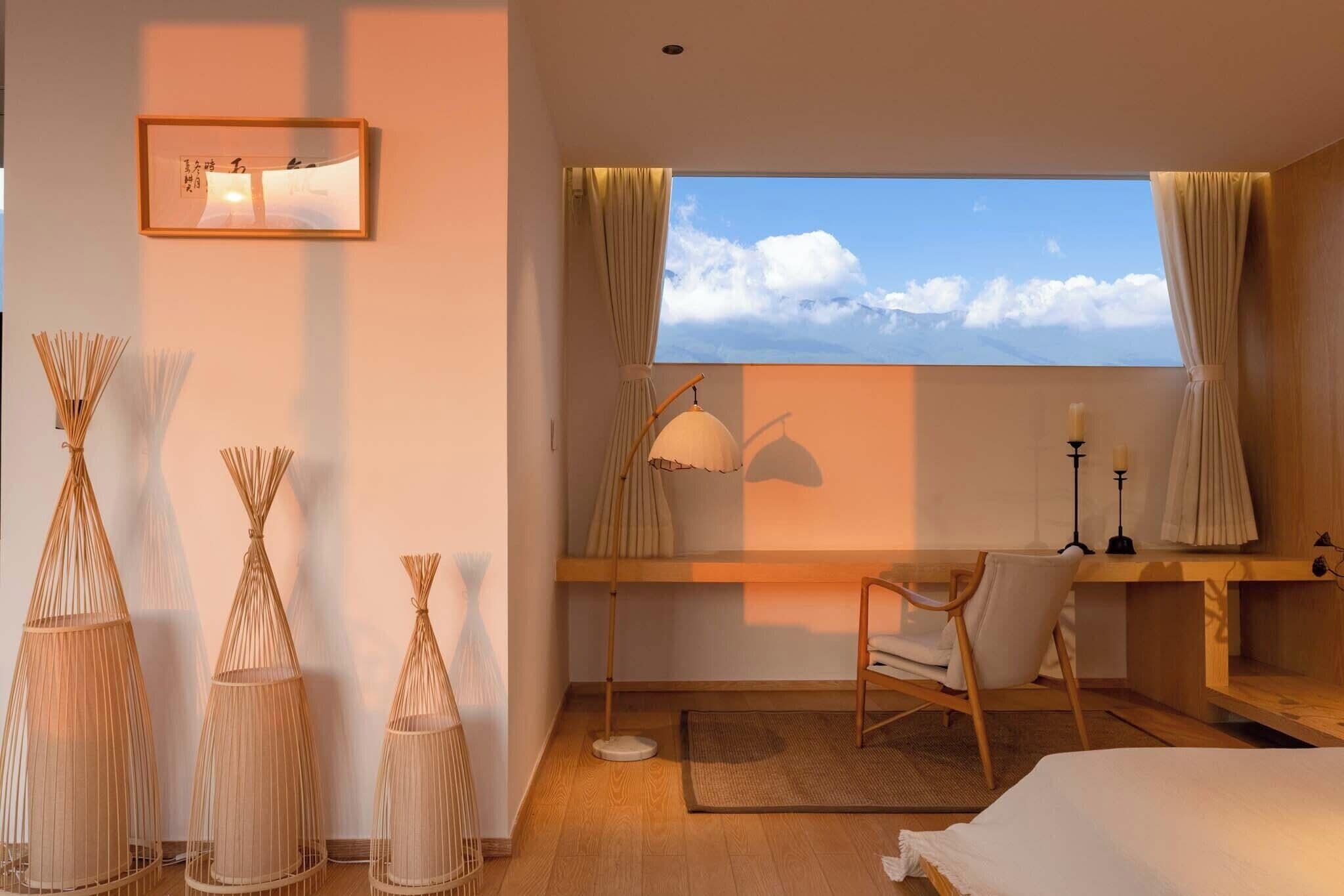 A bedroom with a large window, a desk, a chair, and decorative vases.