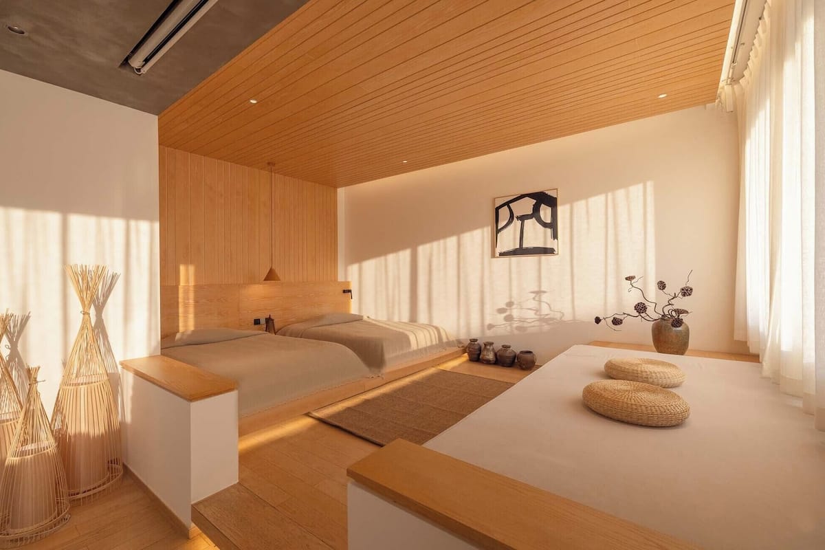 A modern hotel room with a wooden ceiling, a bed, a small table with decorative items, and a wall-mounted artwork.