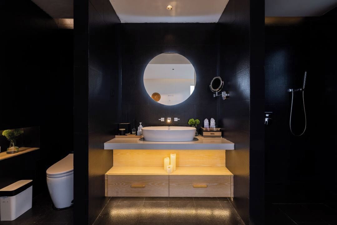Un baño moderno con un espejo redondo, un lavamanos grande, muebles de madera y una ducha.