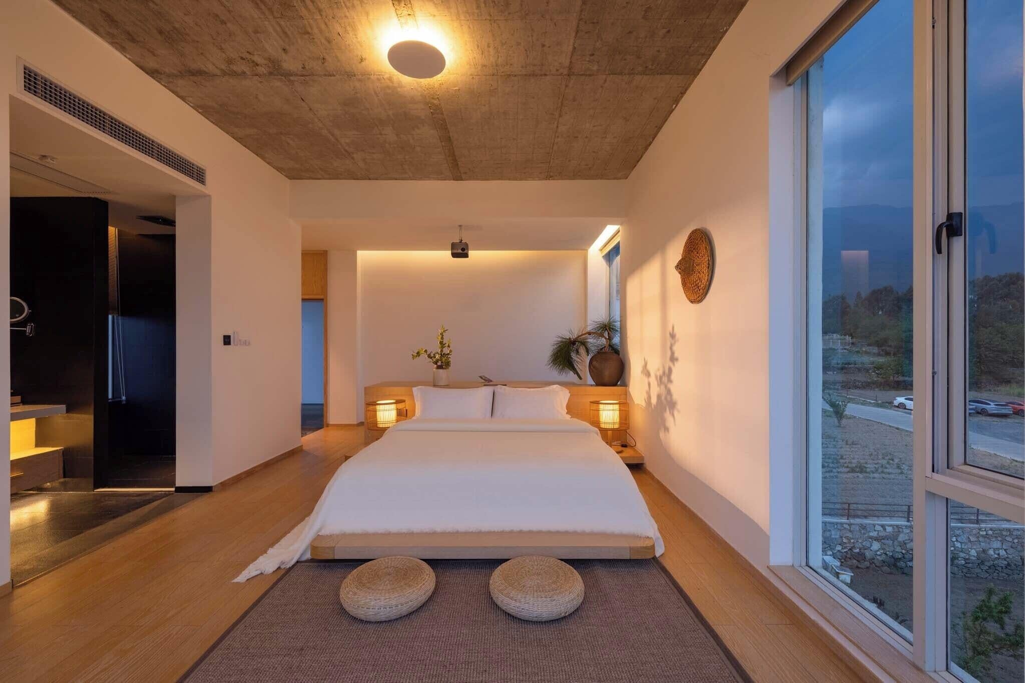 Un dormitorio moderno con una cama grande, lámparas de noche, un proyector y vistas al exterior.