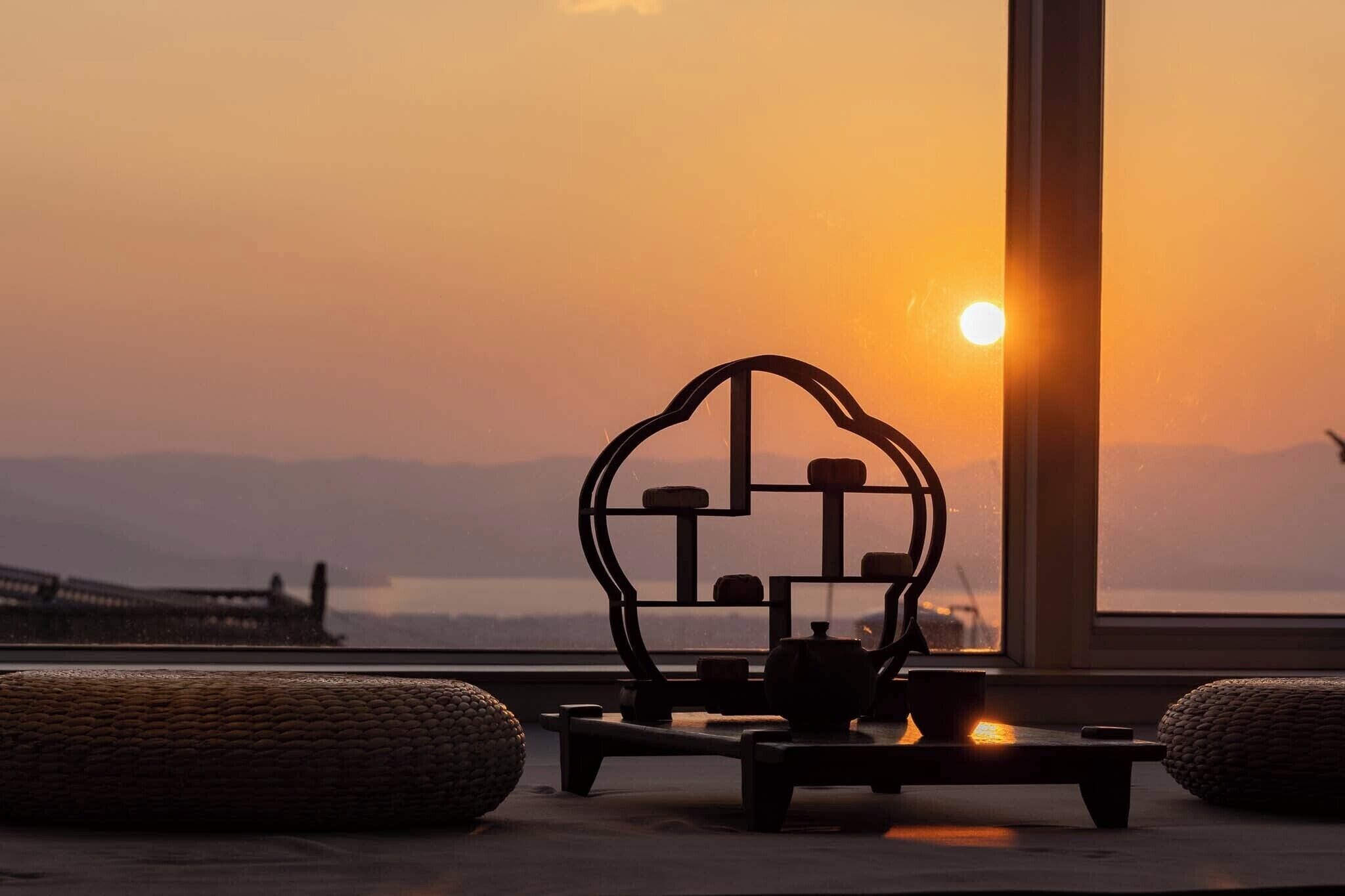 A room with a view of a sunset, a table with a teapot, and a decorative metal piece.