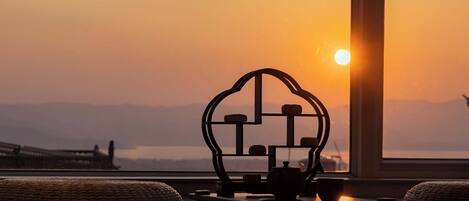A room with a view of a sunset, a table with a teapot, and a decorative metal piece.