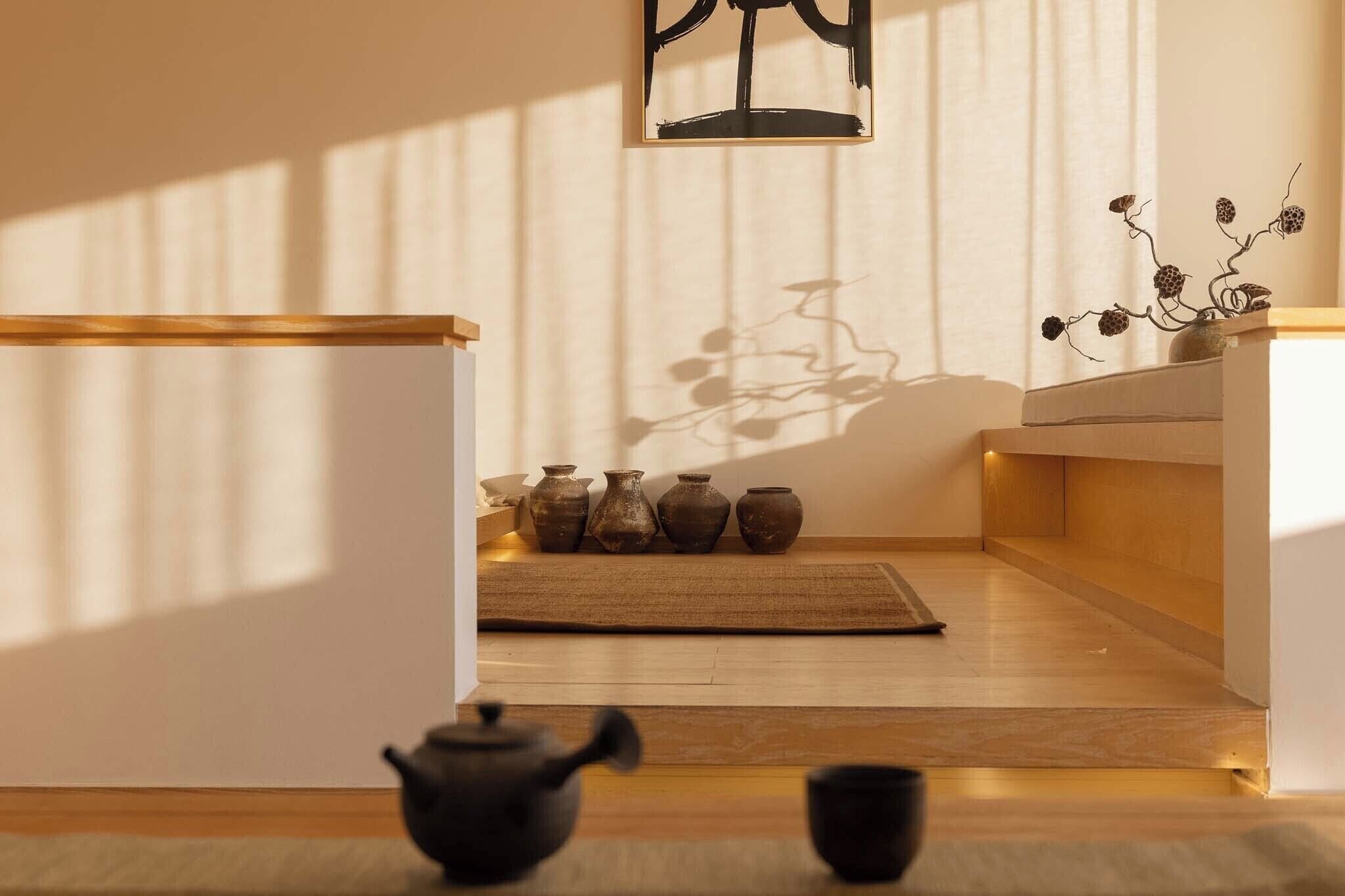 Ein schlichter Raum mit Holzboden, einer Tatami-Matte, einem schwarzen Teekessel und mehreren Keramikvasen.